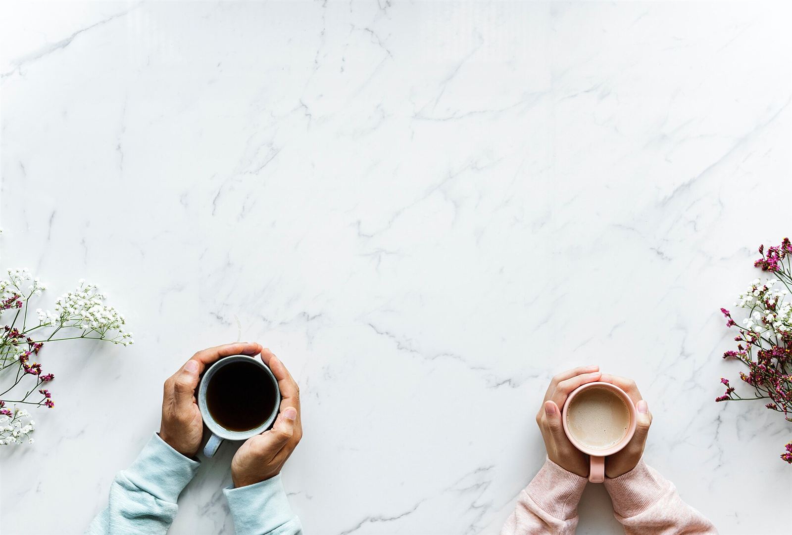 Two people holding warm mugs on a kitchen table